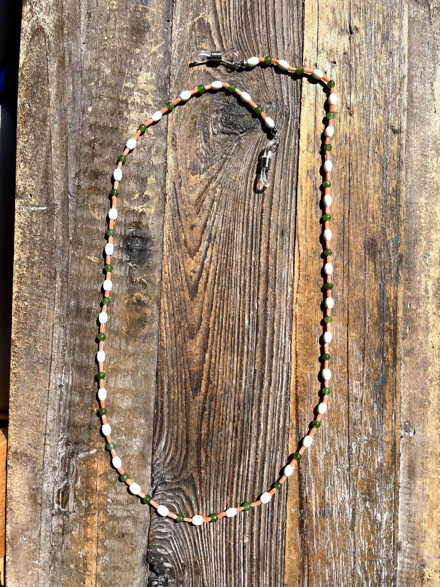 Long beaded mask or eyeglass holder featuring white bone beads green jade beads and coral beads on a wooden surface.