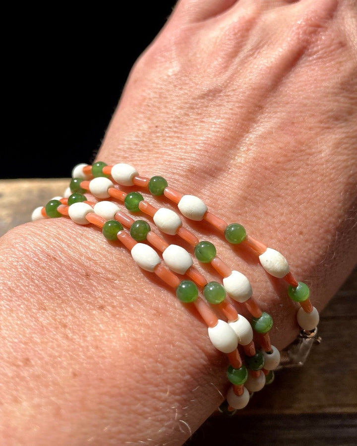 Wrist wearing a three strand beaded bracelet of coral tube beads white round beads and green beads.