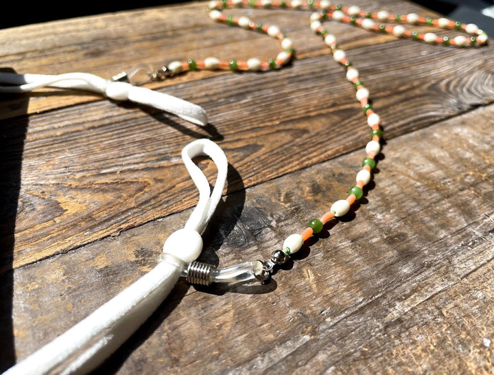 Beaded eyeglass holder with jade green white bone and orange coral beads on a wood surface