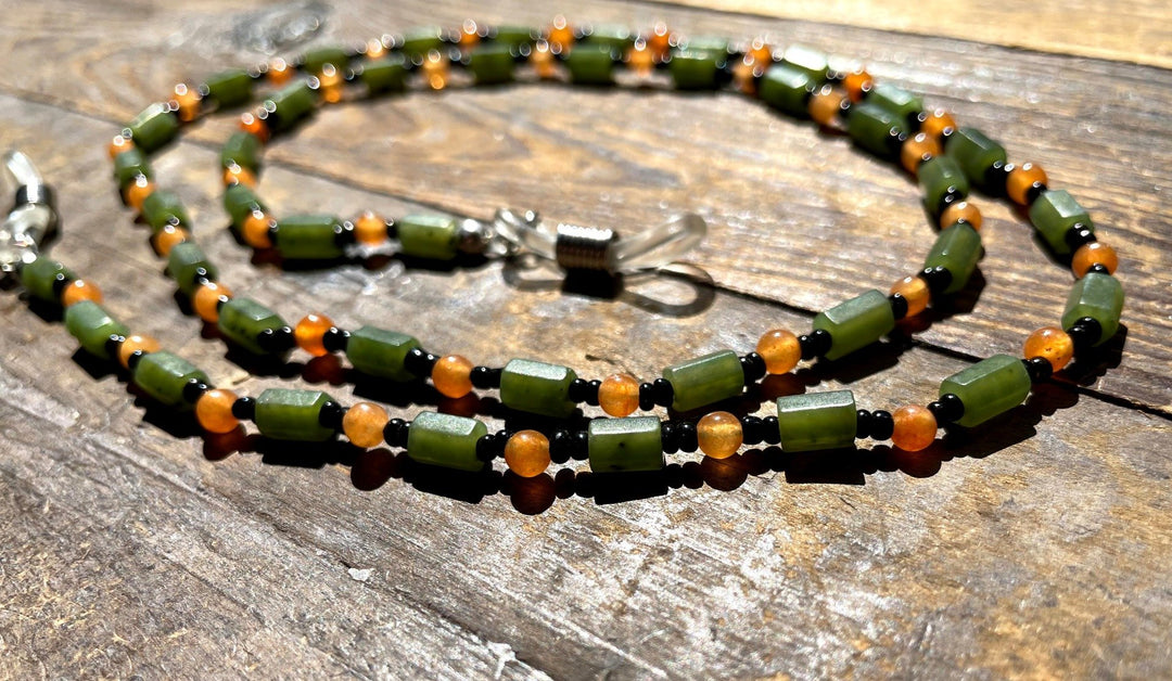 Jade and carnelian eyeglass holder with green cylindrical jade beads and orange rounds on a wooden surface.