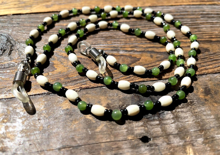 Jade and bone eyeglass holder with white bone beads green jade rounds and black spacers on a rustic wood surface.