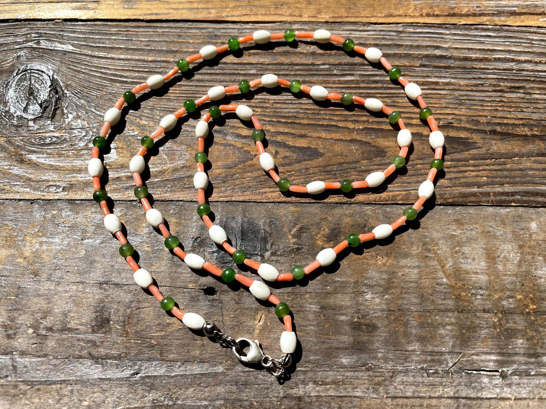Beaded jade necklace with white oval beads green round beads and orange spacers on a rustic wood surface