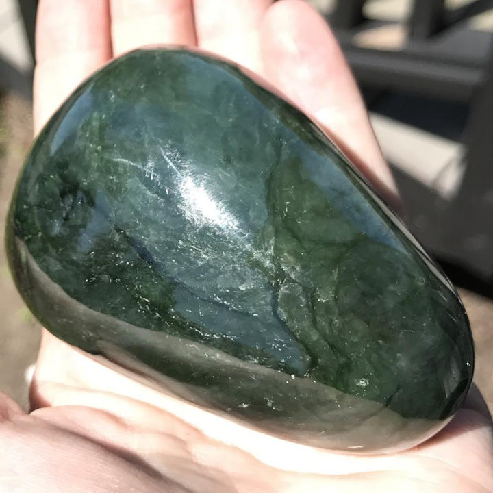 Dark green jade specimen with a smooth glossy finish and subtle white veining held in hand