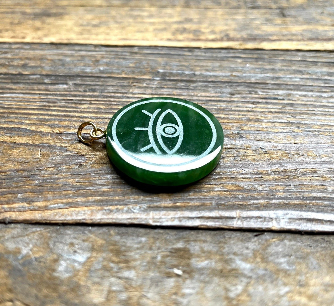 Green circular Canadian jade evil eye pendant with white engraving on rustic wood