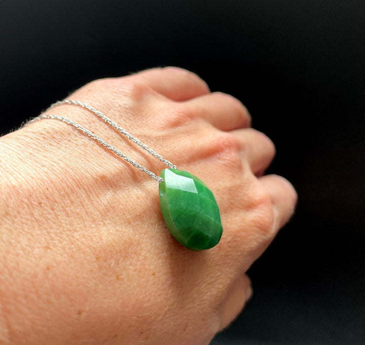 Teardrop green faceted pendant on a silver chain worn on a hand against a dark background