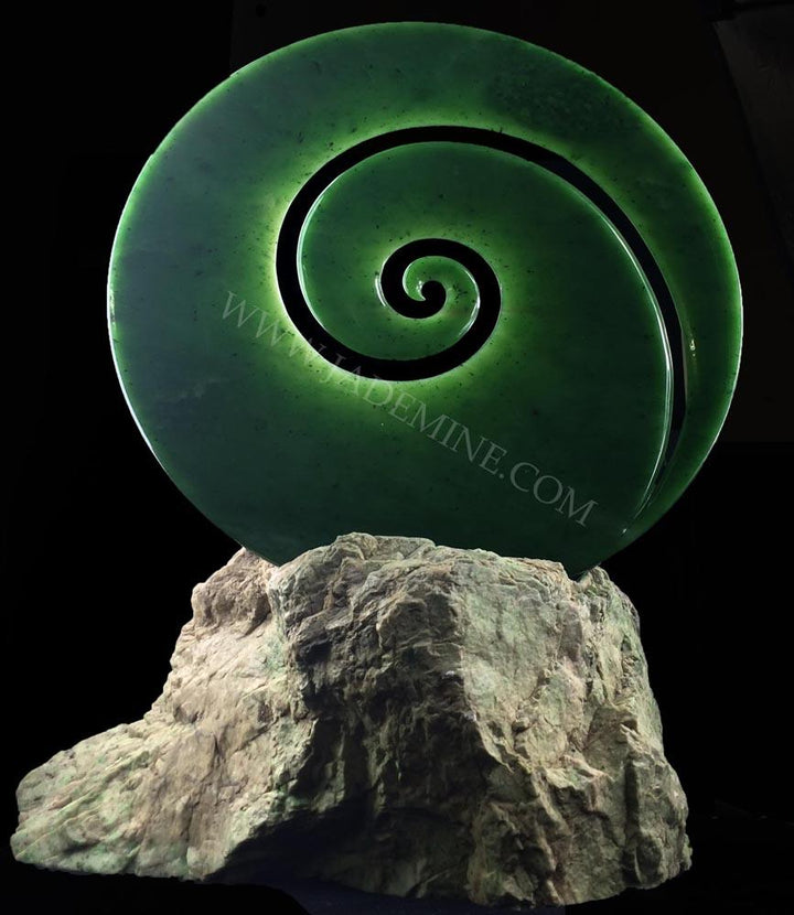 Glowing green spiral sculpture with inner rings perched on a rock pedestal against a black background