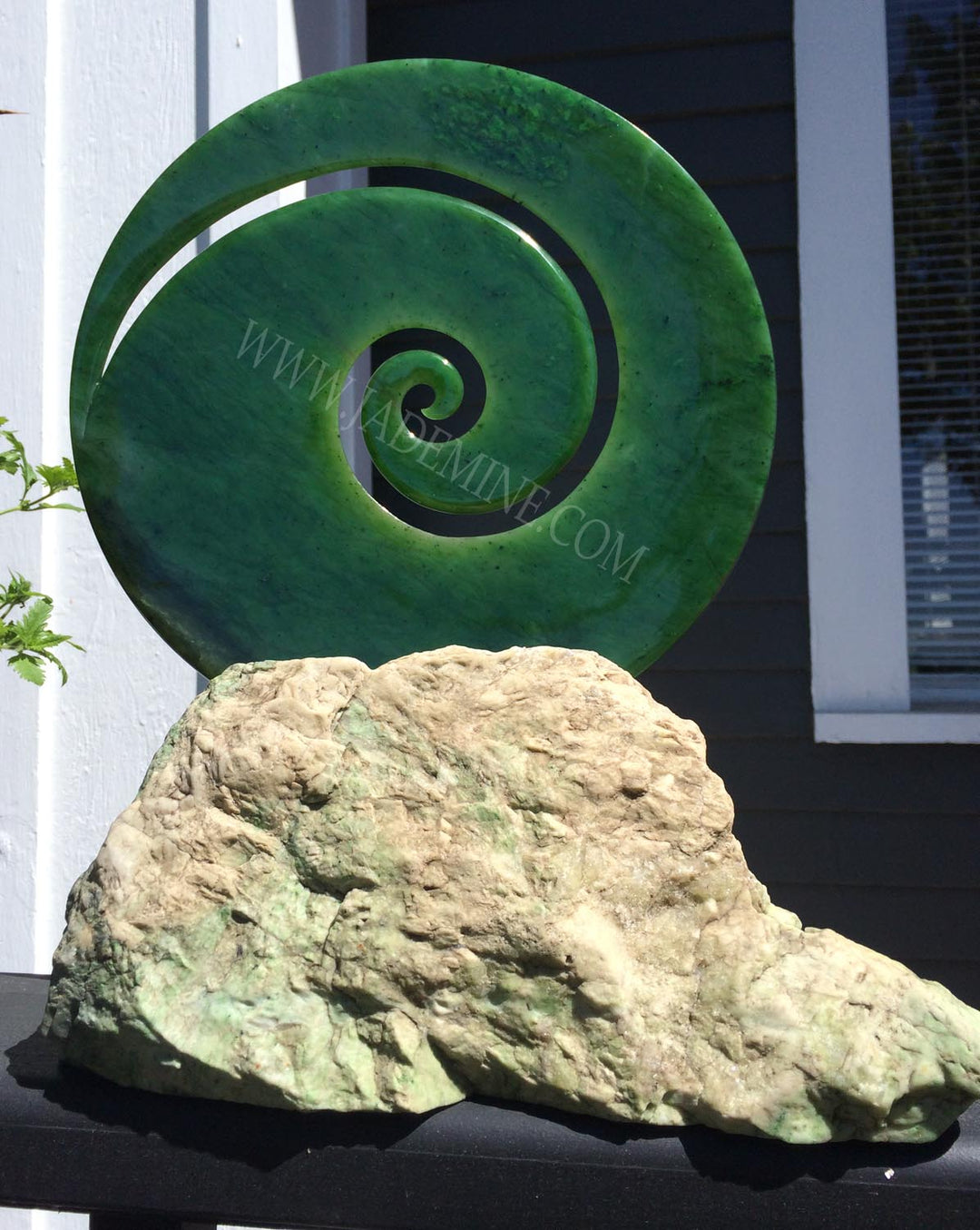 Green spiral sculpture perched on a rugged rock base outdoors