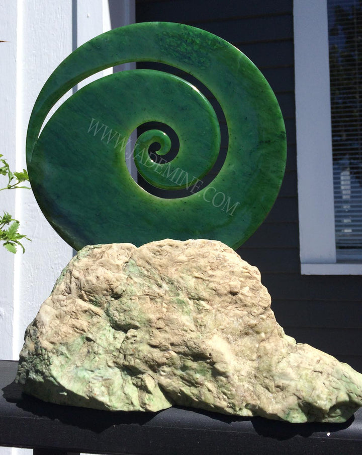 Green spiral sculpture perched on a rugged rock base outdoors