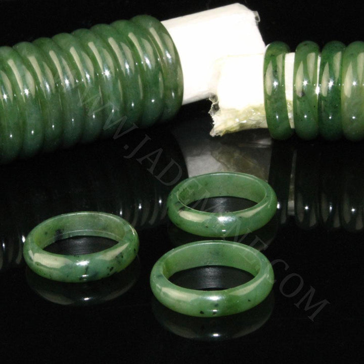 Three 5mm narrow jade band rings on a black reflective surface with a jade bead strand in the background