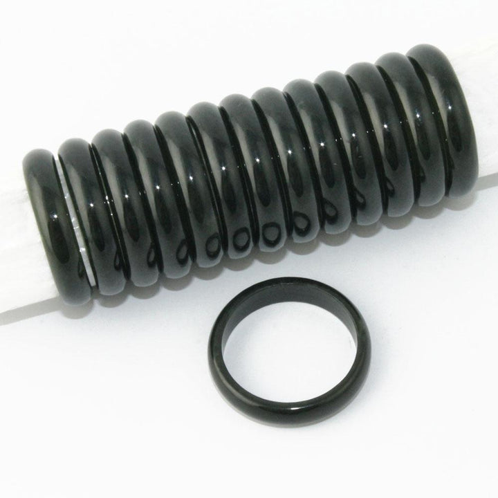 Row of glossy black jade ring spacers on a rod with a single ring placed nearby.