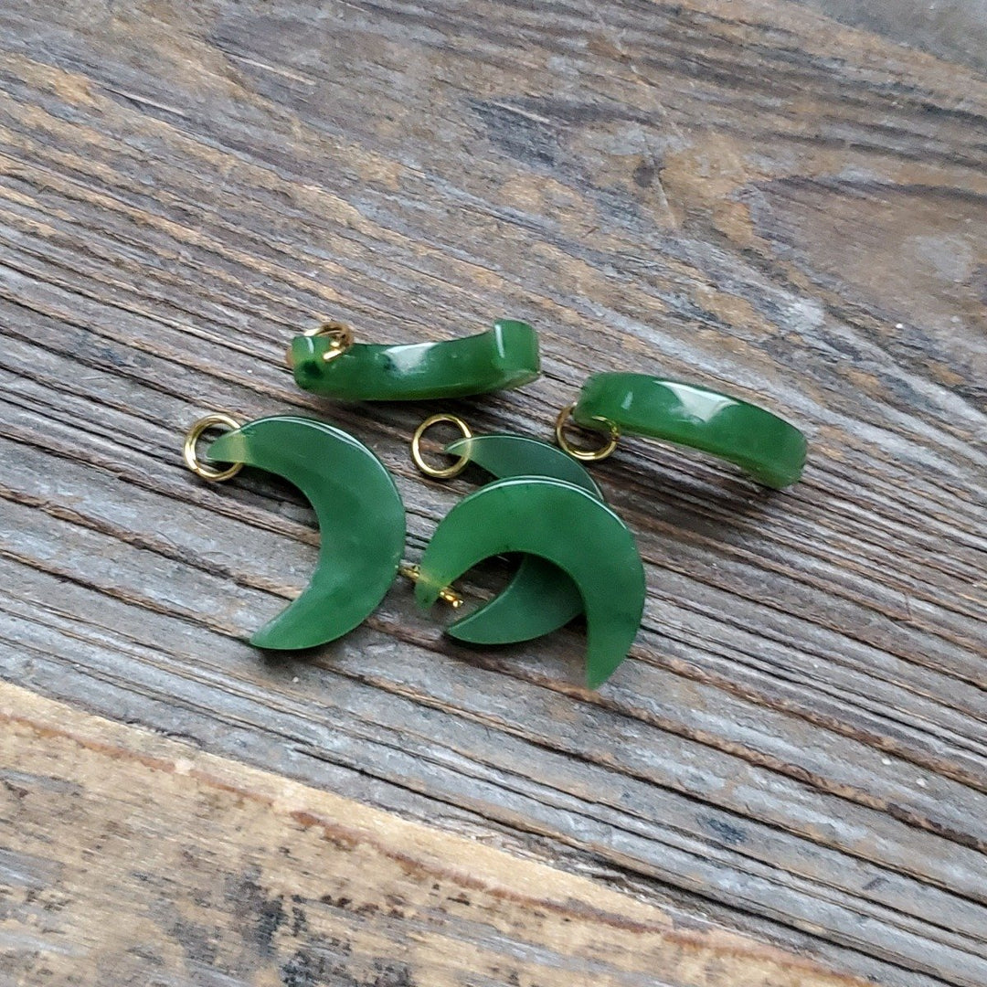 Set of green crescent moon charms with gold loops arranged on a wooden surface.