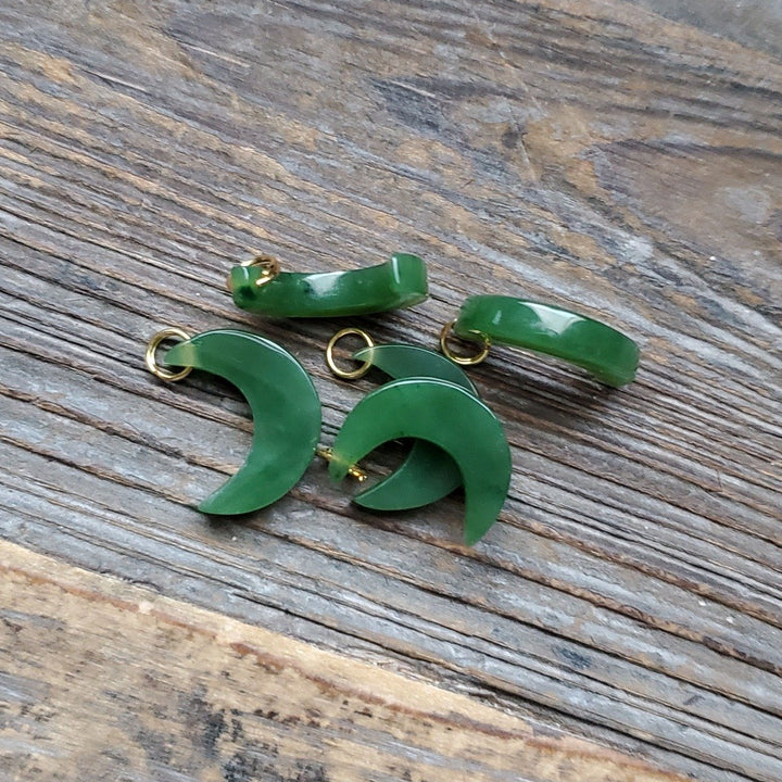 Set of green crescent moon charms with gold loops arranged on a wooden surface.