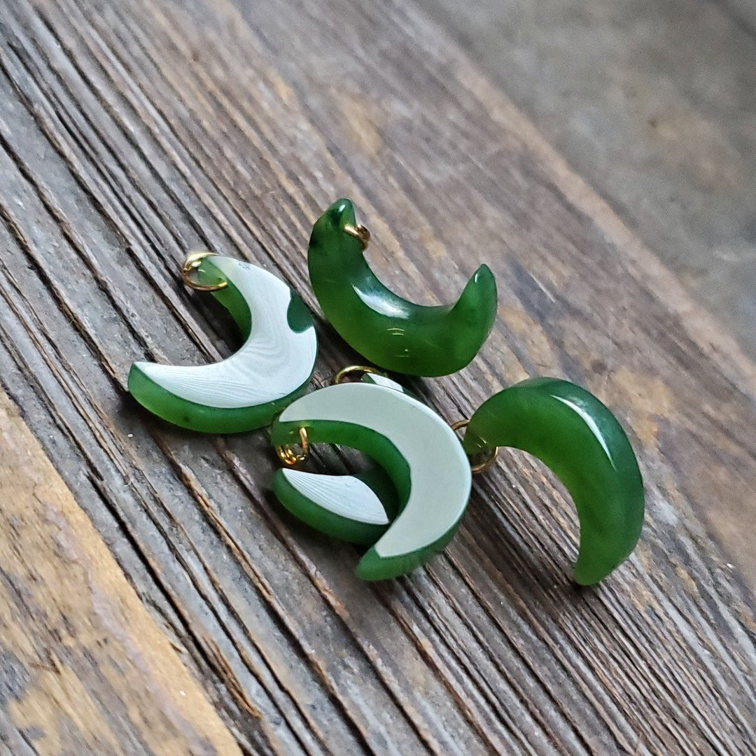 Green and white enamel crescent moon charms with gold loops on a wood surface