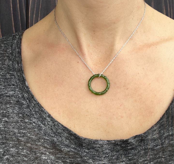 Green jade circular pendant on a silver chain worn at the neck.