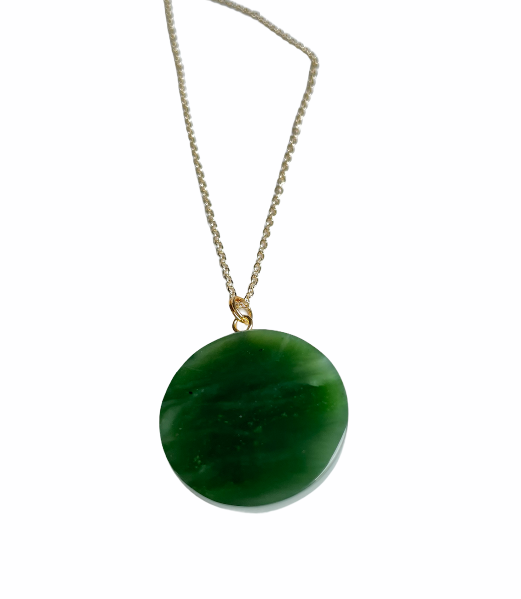 Round Canadian jade evil eye pendant in deep green suspended from a gold bail on a silver chain