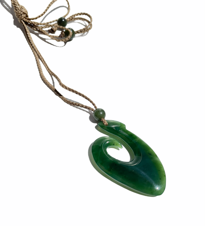 Canadian Jade fish hook pendant displayed on a tan cord with bead, shown from a side angled view.