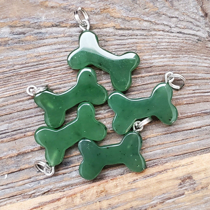 Collection of five green dog bone charms with silver loops spread on a rustic wooden surface.