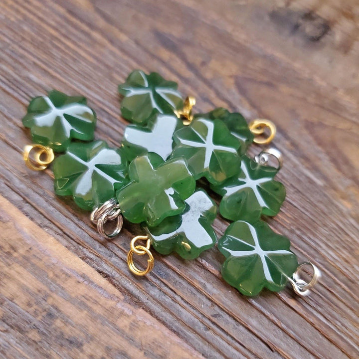 Cluster of green four leaf clover charms with white veins and metal loops on a wooden surface