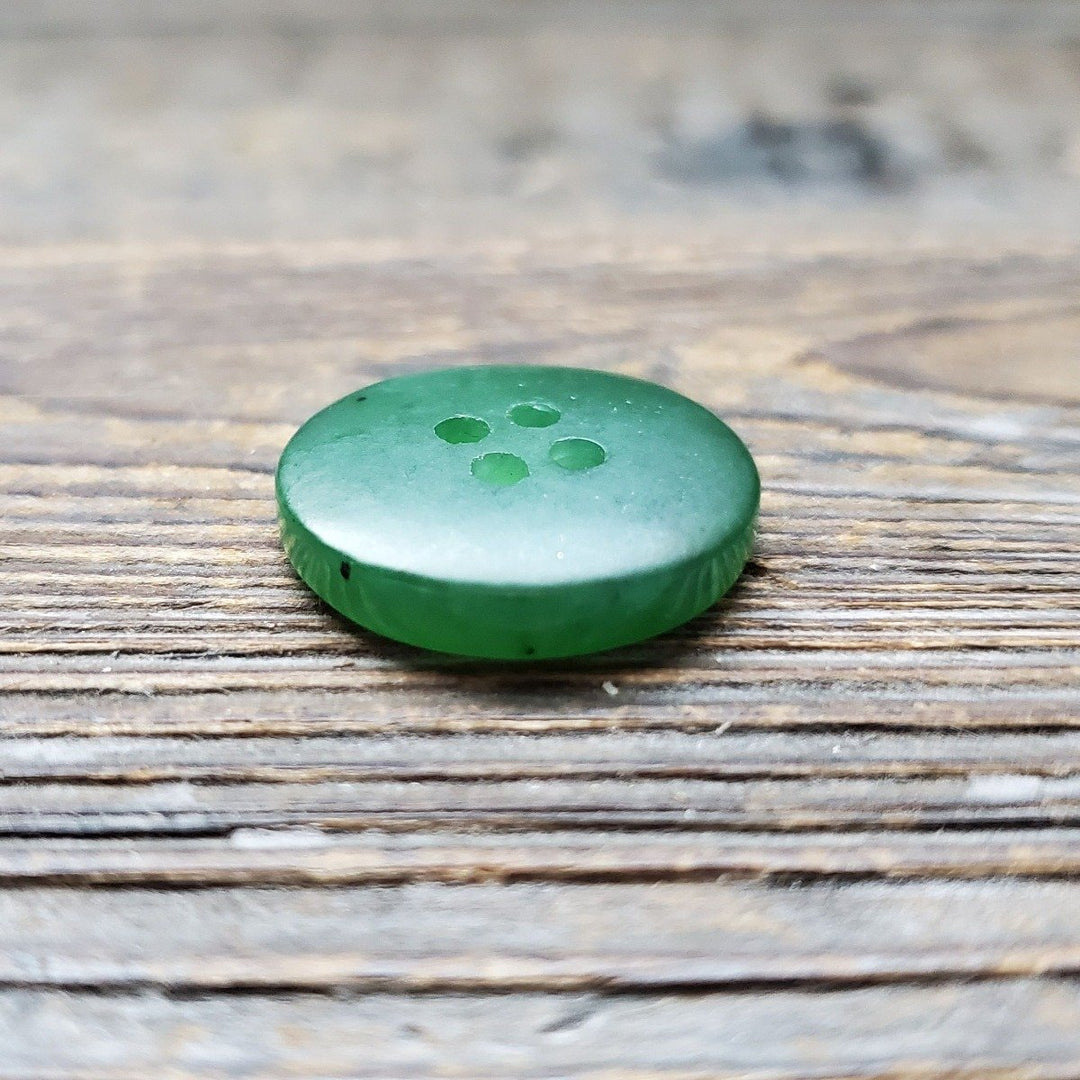 Green jade button with four holes on a weathered wooden surface