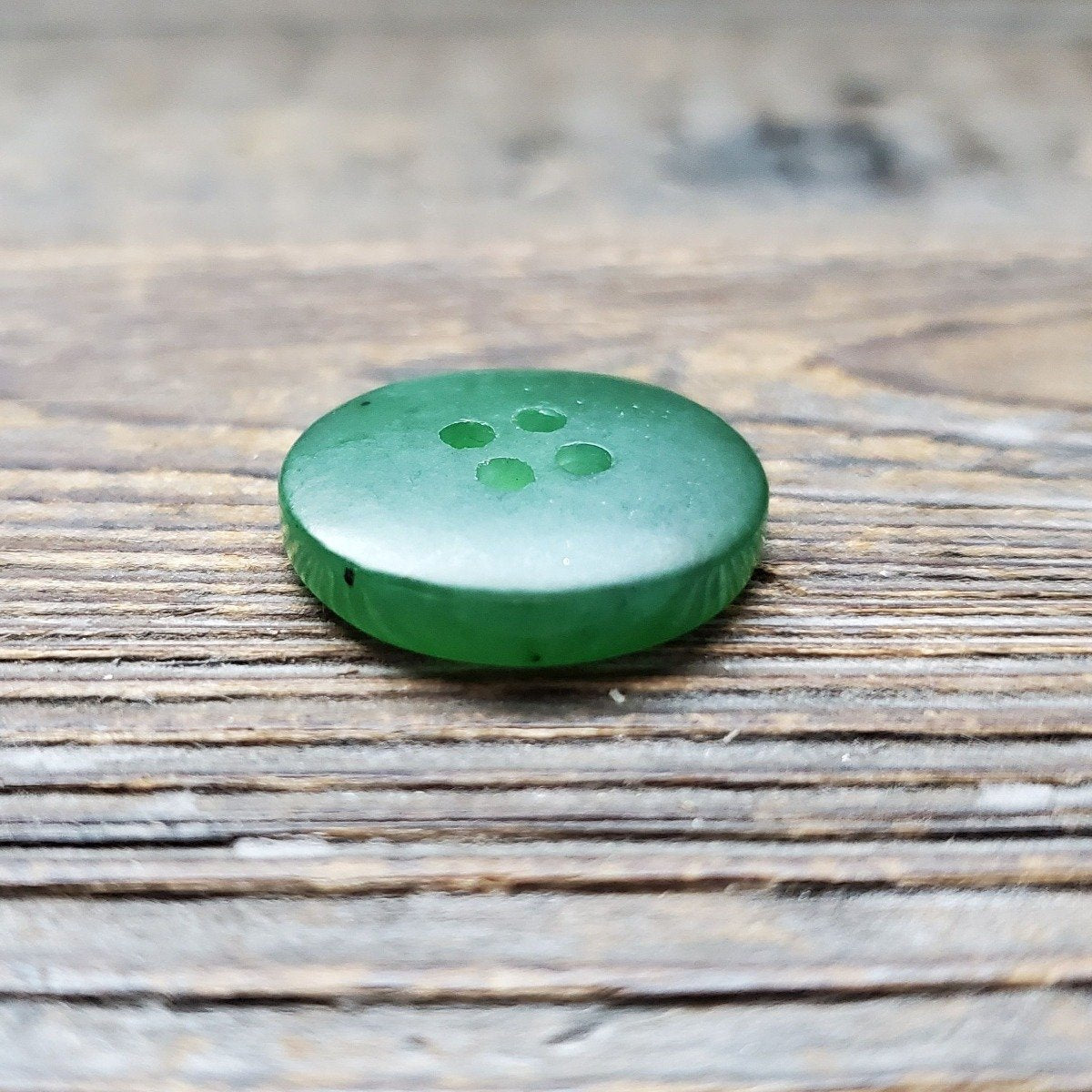 Green jade button with four holes on a weathered wooden surface